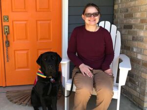 woman sitting in a chair on front of house with a black lab posing next to her