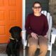 woman sitting in a chair on front of house with a black lab posing next to her
