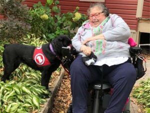 woman using motorized scooter with black lab wearing a red cape