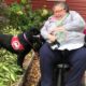 woman using motorized scooter with black lab wearing a red cape