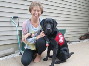 woman kneeling down next to a black lab wearing a red cape