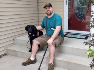 man sitting on a stoop with a black lab next to him
