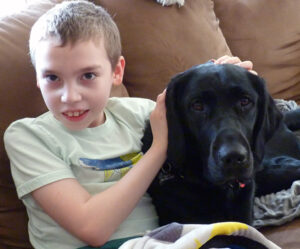 boy sitting on sofa with black dog