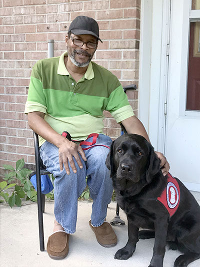 man sitting outside with black service dog