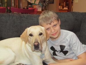 boy poses next to yellow lab together on the couch.