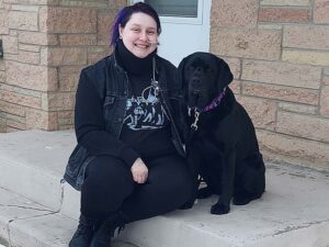 person sits on steps of home with a black dog