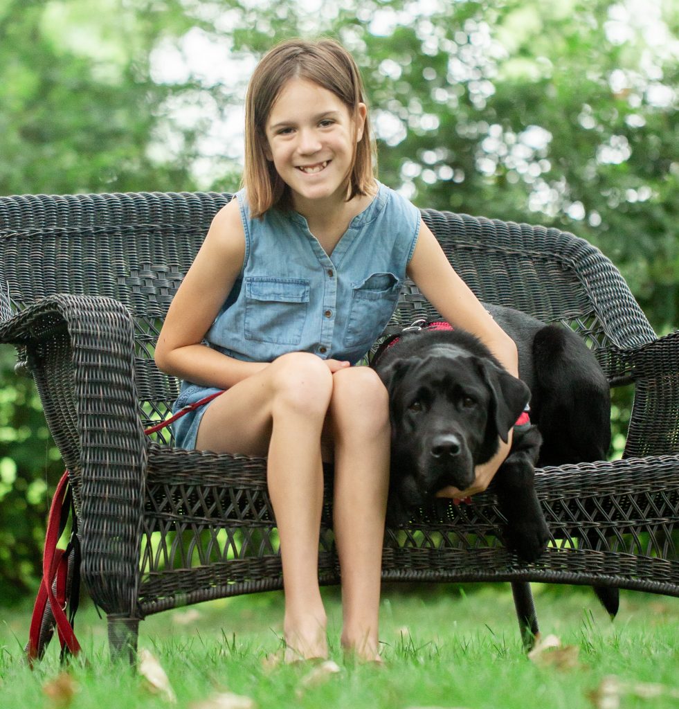 girls and black dog sitting on outside bench