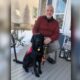 man poses with black lab on the back porch