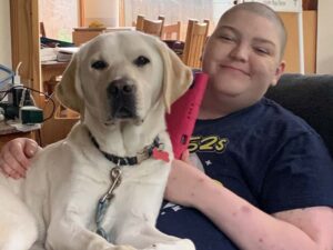 woman and yellow lab sit on a chair together. Both are looking at the camera.