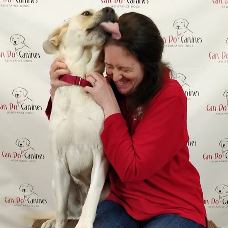 Julianne Larsen sitting with a dog and the dog is licking the top of her head