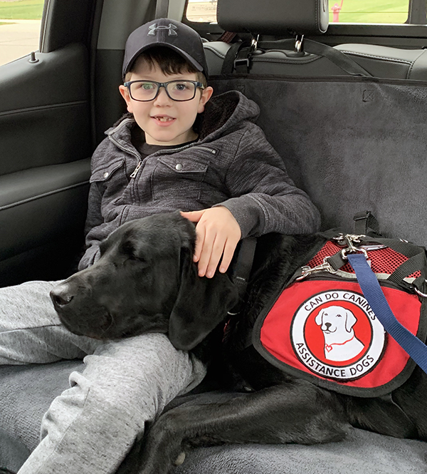 boy and black Lab service dog sitting in back seat of car