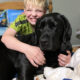 boy with big smile hugging large black dog on bed