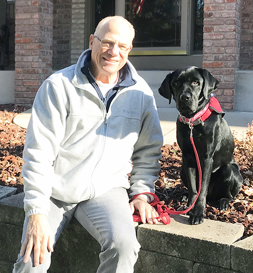 man and black dog sitting on concrete barrier outside home