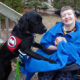 boy in wheelchair with large black service dog putting front paws on him