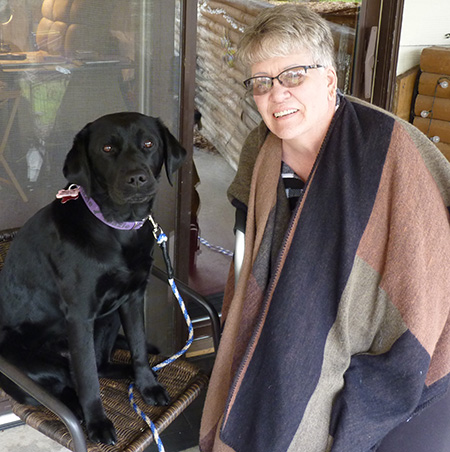 woman standing next to large black dog sitting on patio chair