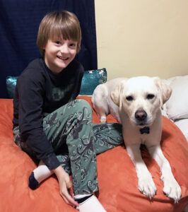 boy and large white dog sitting together on bed