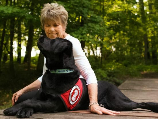 woman sitting outside and looking into eyes of large black service dog