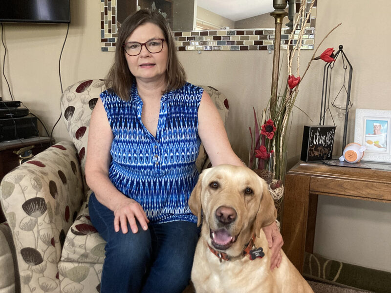 woman in blue blouse sitting in chair with large yellow dog sitting on floor in front of her