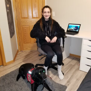teenage girls sitting at desk with laptop open behind her and service dog lying at her feet