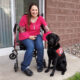 woman sitting on outdoor patio in wheelchair next to service dog