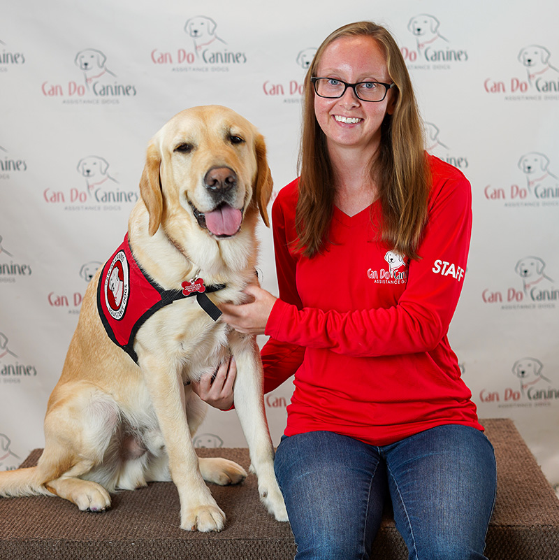 woman with long hair and glasses sitting next to service dog