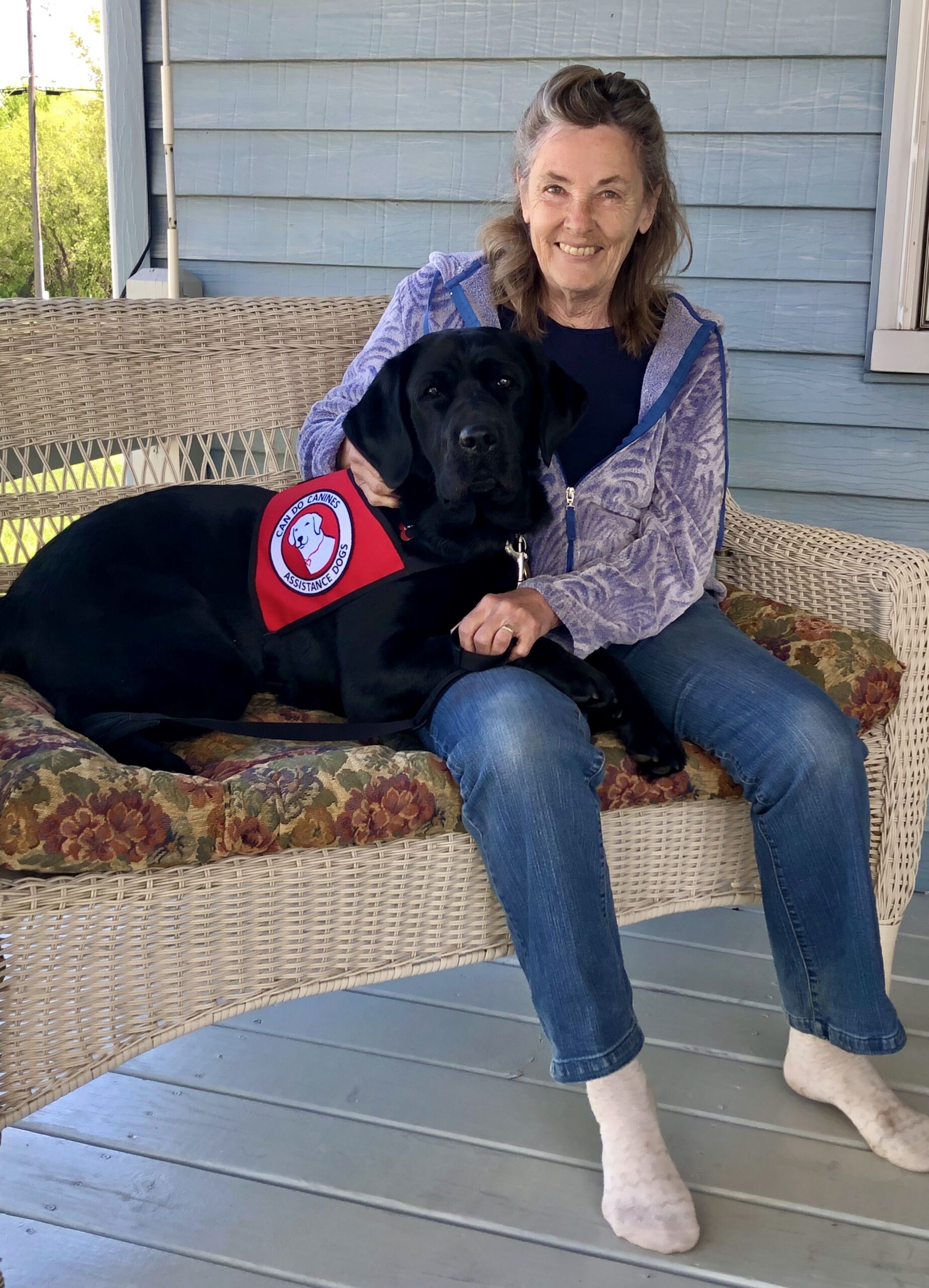 woman sitting on front step with black service dog lying across her lap