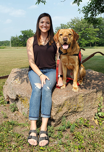 young woman and yellow Lab service dog sitting on large rock