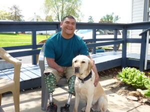 man with amputated legs and hand sitting in lawn chair next to yellow Lab dog