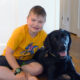 boy sitting on floor in home hugging large black dog
