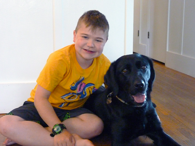 boy sitting on floor in home hugging large black dog