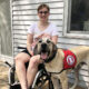 woman sitting in wheelchair on deck with Great Dane service dog standing next to her