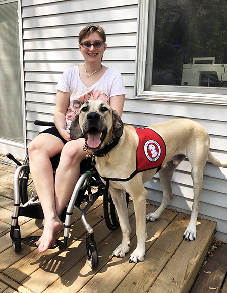 woman sitting in wheelchair on deck with Great Dane service dog standing next to her