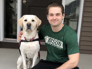 young man in green t-shirt sitting on front porch step next to white service dog