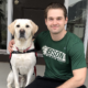 young man in green t-shirt sitting on front porch step next to white service dog