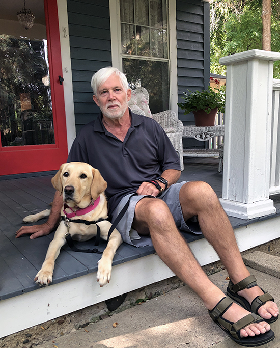 man sitting on front porch step next to yellow Lab service dog
