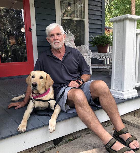 man sitting on front porch step next to yellow Lab service dog