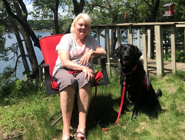 woman sitting outside in red chair with large black dog sitting on grass next to her