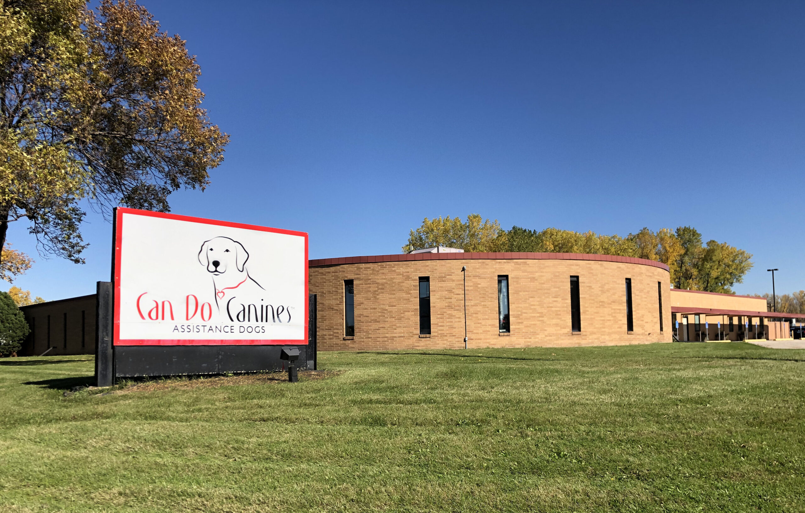 building with sign that says "Can Do Canines Assitance Dogs" on grass in front