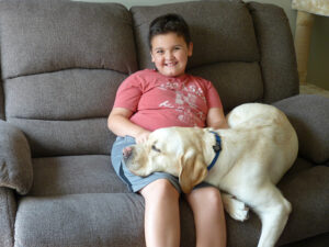 boy sitting on couch with yellow Lab lying next to him with dog's head on his lap