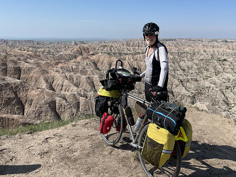man in bike gear and helmet standing with bike along side of canyon