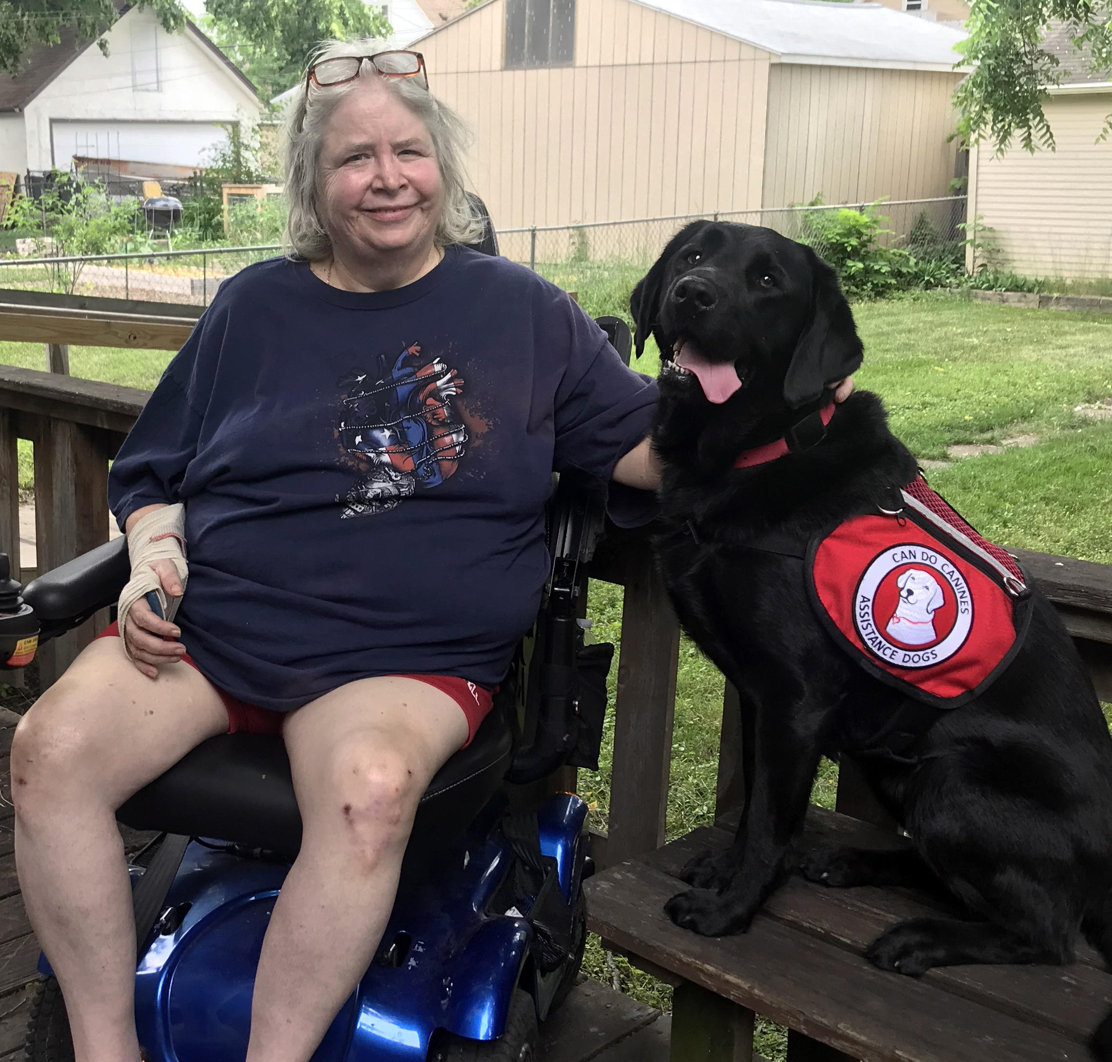 woman sitting in wheelchair on deck next to black service dog