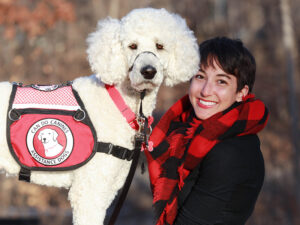 young woman sitting with face next to white poodle service dog