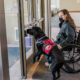 black dog wearing Can Do Canines service dog cape pressing door pushplate for young man in wheelchair