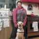 Young woman standing in kitchen with yellow Lab service dog in sitting in front of her