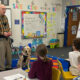 man standing in front of classroom of kids with yellow Lab service dog sitting at his side