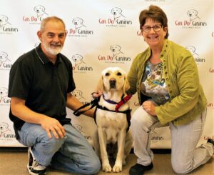 man and woman kneeling around a yellow Lab wearing a red Can Do Canines service dog cape