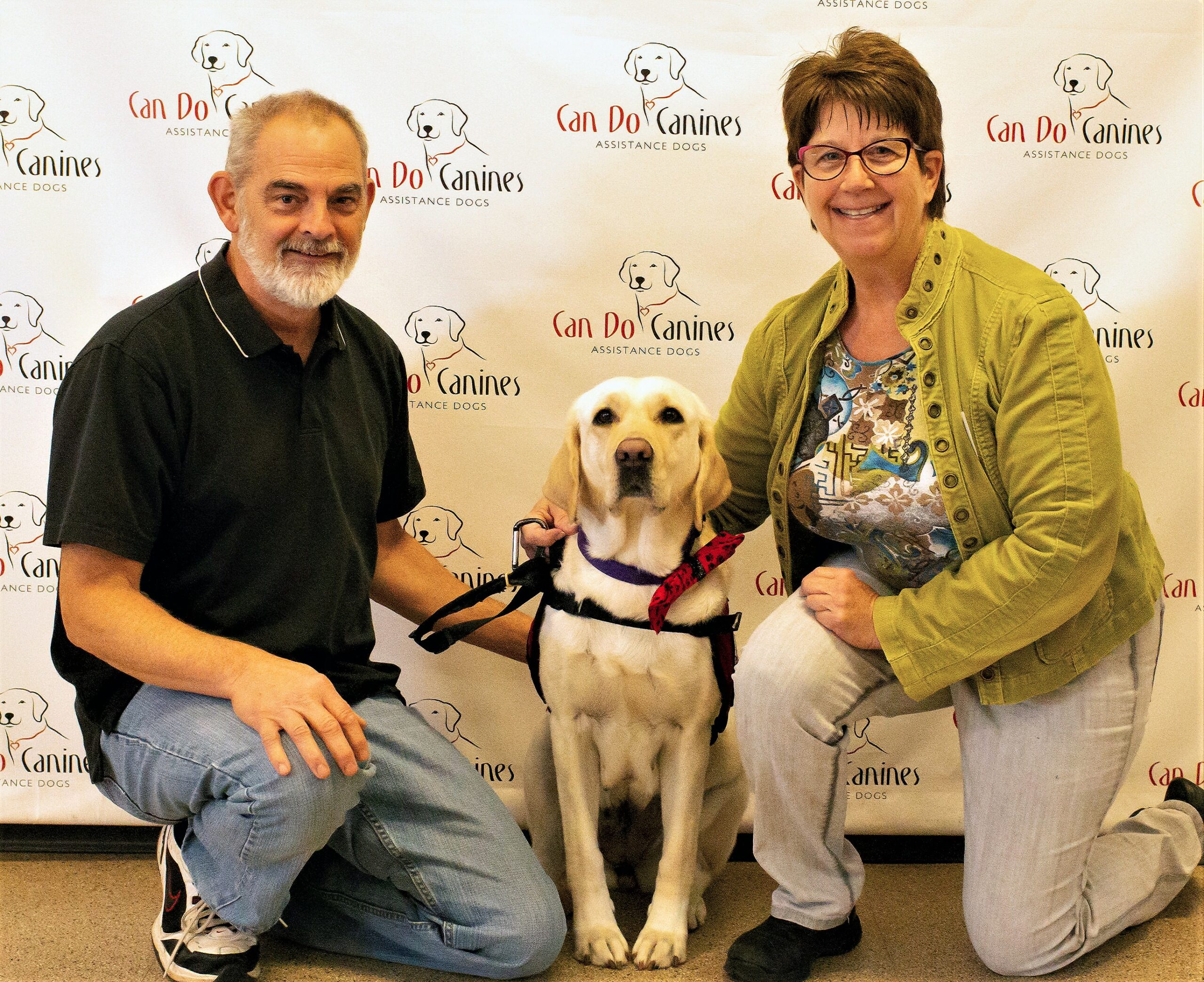 man and woman kneeling around a yellow Lab wearing a red Can Do Canines service dog cape