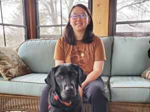 young woman sitting on sofa with black Lab sitting on floor in front of her