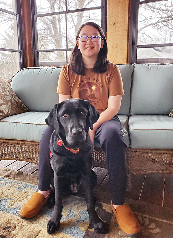 young woman sitting on sofa with black Lab sitting on floor in front of her