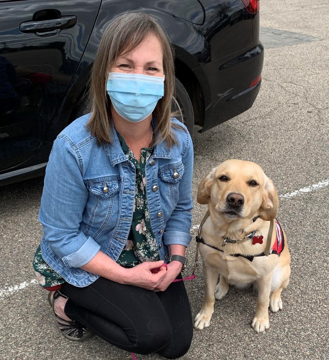 Woman kneeling next to a yellow lab in a red Can Do Canines cape.